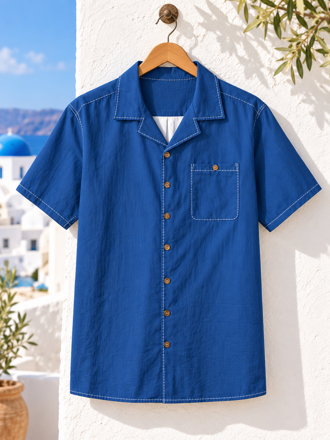 Aegean Escape royal-blue shirt on wooden hanger overlooking Santorini